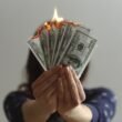 Apps like Dave and EarnIn: hands holding burning dollar bills showing the real cost of cash advances