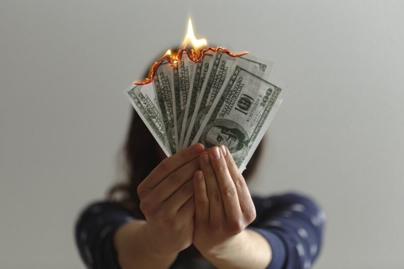Apps like Dave and EarnIn: hands holding burning dollar bills showing the real cost of cash advances